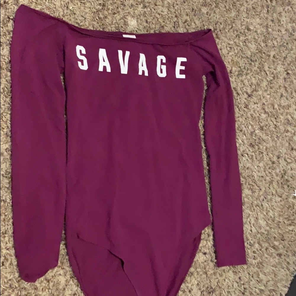 Purple body suit, low shoulder, “savage” on front